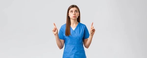 Sağlık çalışanları, virüsü önleyin, covid-19 test taraması, tıp konsepti. Aptal üzgün doktor, mavi önlüklü bayan hemşire hayal kırıklığına uğramış, işaret ediyor ve rahatsız edici bir şekilde yukarı bakıyor. — Stok fotoğraf