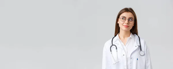 Медицинские работники, медицина, страхование и концепция пандемии ковида-19. Мечтательный молодой талантливый доктор в белых халатах и очках, задумчивый и улыбающийся в верхнем левом углу, представляющий что-то — стоковое фото