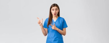 Sağlık çalışanları, virüsü, sigortayı ve ilaç konseptini engelleyin. Şaşırmış hemşire ya da doktor mavi önlüklü, ağzı açık ve kameraya bakıyor, parmaklarını sola şaşkın bir şekilde gösteriyor.