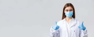 Covid-19, virüsü önleme, sağlık çalışanları ve karantina konsepti. Neşeli kadın doktor, beyaz önlüklü ve lastik eldivenli doktor, baş parmağını kaldır, korona enfeksiyonuna karşı koruma iste.