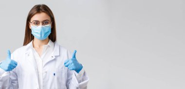 Covid-19, virüsü önleme, sağlık çalışanları ve karantina konsepti. Neşeli kadın doktor, beyaz önlüklü ve lastik eldivenli doktor, baş parmağını kaldır, korona enfeksiyonuna karşı koruma iste.