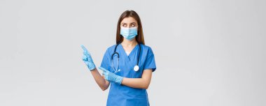 Covid-19, virüsün önlenmesi, sağlık, sağlık çalışanları ve karantina konsepti. Doktor, tıbbi maskeli ve mavi önlüklü kadın hemşire, Coronavirus bilgileriyle bayrağa bakıyor ve onu işaret ediyor.
