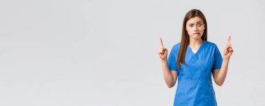 Sağlık çalışanları, virüsü, sigortayı ve ilaç konseptini engelleyin. Endişeli ya da gergin hemşire ya da doktor mavi önlüklü, ısıran dudaklı endişeli, yukarı bakan, baştan çıkarıcı, gri arka planlı