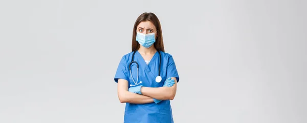 Covid-19, virüsün önlenmesi, sağlık, sağlık çalışanları ve karantina konsepti. Mavi önlüklü, steteskoplu ve kişisel koruyucu ekipmanlı şüpheli ve endişeli bayan hemşire şüpheli görünüyor. — Stok fotoğraf