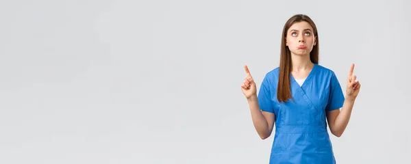 Trabajadores de la salud, prevenir virus, pruebas de detección de covid-19, concepto de medicina. tonto molesto lindo doctor, mujer enfermera en azul scrubs puching decepcionado, apuntando y mirando hacia arriba disgustado — Foto de Stock