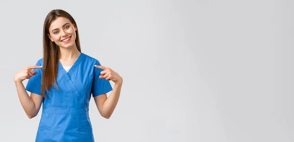 Gezondheidswerkers, voorkomen virus en geneeskunde concept. Vrolijke, lachende mooie dokter, vrouwelijke verpleegster in blauwe scrubs die naar zichzelf wijst, klaar om patiënten te helpen, levens te redden van het coronavirus. — Stockfoto