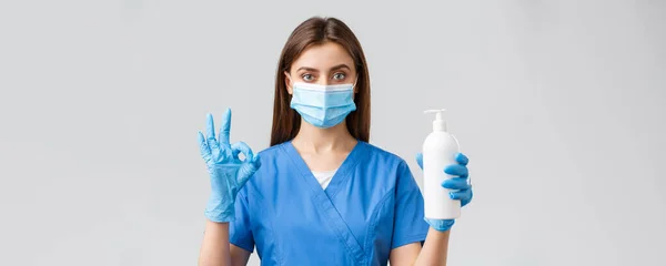 Covid-19, megelőzés vírus, egészségügyi dolgozók és karantén koncepció. Magabiztos, komoly női nővér, csinos orvos műtősruhában és orvosi maszkban, kézfertőtlenítő, szappan és oké jel. — Stock Fotó