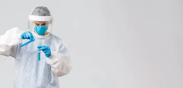Covid-19, 의학 연구, 의료 종사자 및 격리 개념. 코로나 바이러스 백신을 개발하고 있는 병원의 실험실 의사가 다른 시험관에 액체를 붓고 개인용 보호용 의상을 입고 있습니다. — 스톡 사진