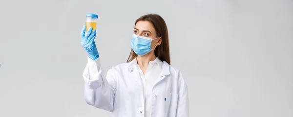 Covid-19, medisch onderzoek, diagnose, gezondheidswerkers concept. Professionele arts in kliniek lab, scrubs en medisch masker, kijken naar urinemonster, patiënt test op coronavirus infectie — Stockfoto