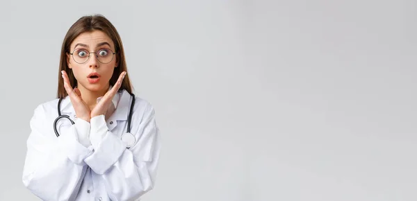 Trabajadores sanitarios, medicina, seguros y concepto de pandemia covid-19. Doctora sorprendida e impresionada en gafas, uniformes blancos, jadeando y mirando asombrada cámara, fondo gris — Foto de Stock