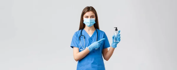 Covid-19, förebyggande av virus, hälsa, vårdpersonal och karantänkoncept. Ung professionell kvinnlig sjuksköterska eller läkare i blå skurar, medicinsk mask, peka finger åt hand desinfektionsmedel — Stockfoto