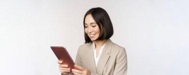 Asyalı iş kadınının dijital tablet kullanması, alete bakması, gülümsemesi, çalışması, beyaz arka plana karşı durması.