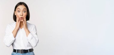 Asyalı kadın modelin görüntüsü şaşırmış, şaşkın şaşkın bakıyor, büyük haberlere tepki veriyor, beyaz arka planda duruyor.