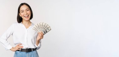 Kredi ve kredi konsepti. Elinde nakit parayla gülümseyen genç Asyalı kadın ve kameraya mutlu bakıyor, beyaz arka plan.