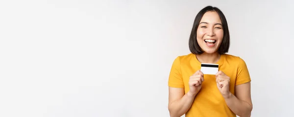 Porträt der schönen Koreanerin mit Kreditkarte, die den Bankservice empfiehlt, im gelben T-Shirt vor weißem Hintergrund — Stockfoto