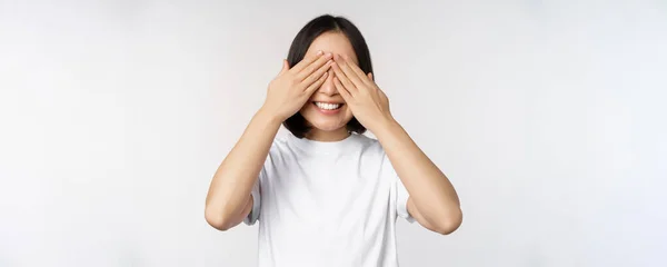 Retrato de mujer asiática cubriendo ojos, esperando sorpresa con los ojos vendados, sonriendo feliz, anticipando, de pie sobre fondo blanco —  Fotos de Stock