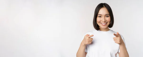 카메라를 향해 손가락 질하고, 선택하고, 축하하고, 하얀 배경 위에 티셔츠를 입고 서 있는 이시아 소녀의 사진 — 스톡 사진