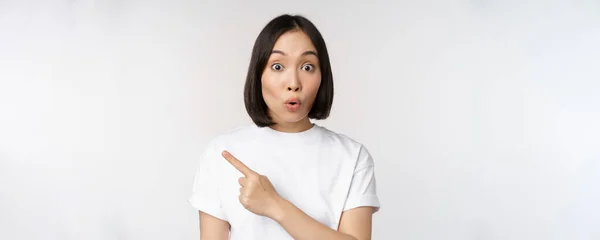 Close-up van jonge japanse vrouw glimlachen, wijzend vinger links op kopieerruimte, tonen aankondiging of reclame banner, staande over witte achtergrond — Stockfoto