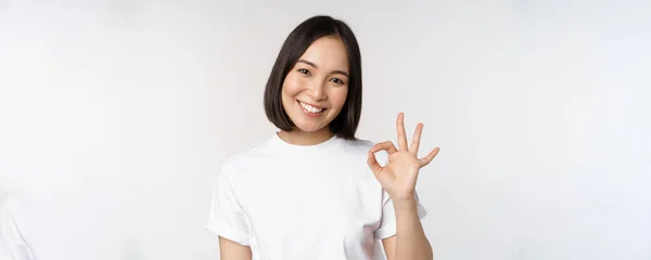 Está tudo bem. Sorrindo jovem asiático mulher assegurando, mostrando ok sinal com rosto satisfeito, de pé sobre fundo branco — Fotografia de Stock