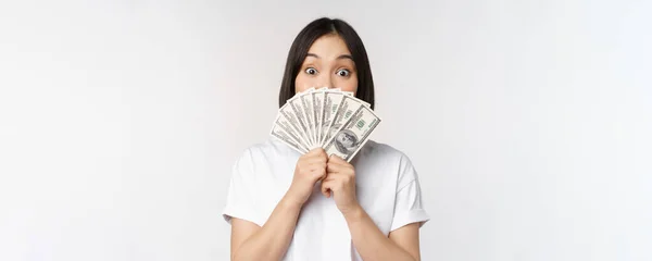 Glad asiatisk flicka som håller pengar, kontanter nära ansiktet, begreppet mikrokrediter och finans, vit studio bakgrund — Stockfoto