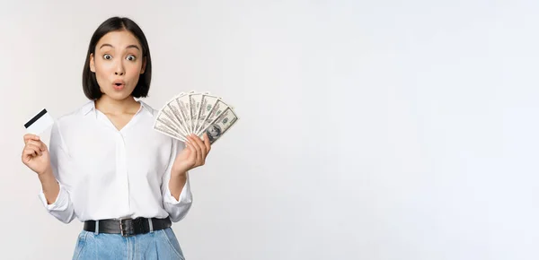 Οικονομική και χρηματική έννοια. Ευτυχισμένη νεαρή Ασιάτισσα που χορεύει με μετρητά και πιστωτική κάρτα, χαμογελώντας ευχαριστημένη, ποζάροντας σε λευκό φόντο στούντιο — Φωτογραφία Αρχείου