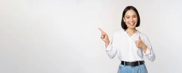 若いアジアのビジネス女性のイメージ,指を左に向けながら笑顔と親指を表示,製品をお勧めします,賞賛,白い背景の上に立って — ストック写真