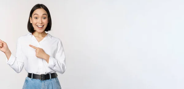 Retrato de mujer asiática joven excitada, señora de la oficina señalando los dedos a la izquierda en el descuento, mostrando banner de venta, de pie sobre fondo blanco — Foto de Stock