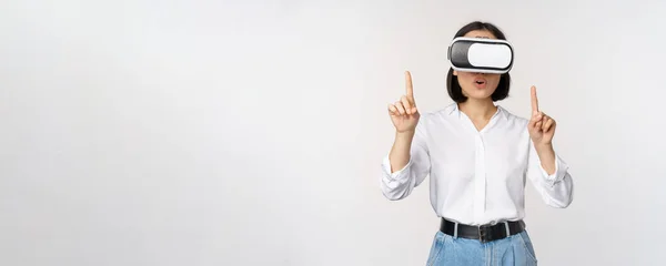 Image de femme asiatique dans des lunettes vr pointant les doigts vers le haut, regardant étonné et surpris. Fille utilisant casque de réalité virtuelle, concept d'avenir et de communication, fond blanc — Photo