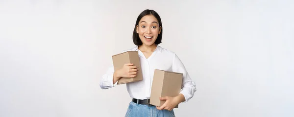 Retrato de menina coreana feliz segurando duas caixas e sorrindo, olhando espantado com a câmera, conceito de compras, fundo branco — Fotografia de Stock