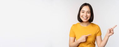 Afallamış genç Asyalı bir kadın, reklam bir yana, terfiyi işaret ediyor. Metni, marka logosunu, beyaz arka planda mutlu duruyor.