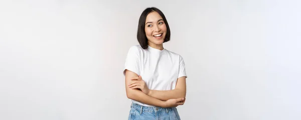 Portret szczęśliwej azjatki uśmiechniętej, pozującej pewnie, krzyżującej ramiona na klatce piersiowej, stojącej na tle studia — Zdjęcie stockowe