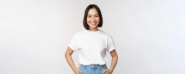Стиль жизни. Счастливая современная девушка, улыбающаяся и счастливо выглядящая перед камерой, позирующая в белой футболке и джинсах, на фоне студии — стоковое фото