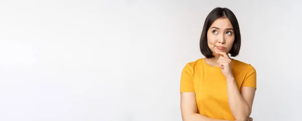 Beeld van het denken aziatische vrouw, kijken opzij en nadenken, het maken van beslissing, staan in geel tshirt over witte achtergrond — Stockfoto