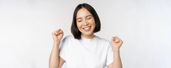 Tanzendes asiatisches Mädchen, das feiert, sich glücklich und optimistisch fühlt, breit lächelt, vor weißem Studiohintergrund steht — Stockfoto
