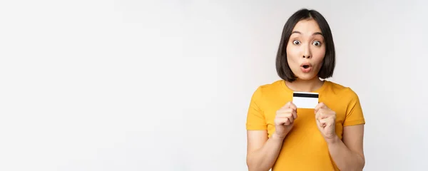 Retrato de bela menina coreana segurando cartão de crédito, recomendando serviço bancário, de pé em camiseta amarela sobre fundo branco — Fotografia de Stock