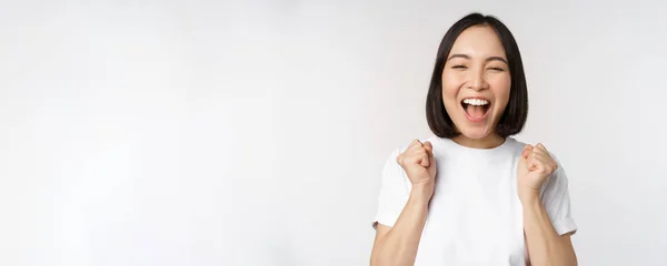 Retrato de mujer asiática entusiasta ganando, celebrando y triunfando, levantando las manos, lograr la meta o el éxito, de pie sobre fondo blanco — Foto de Stock