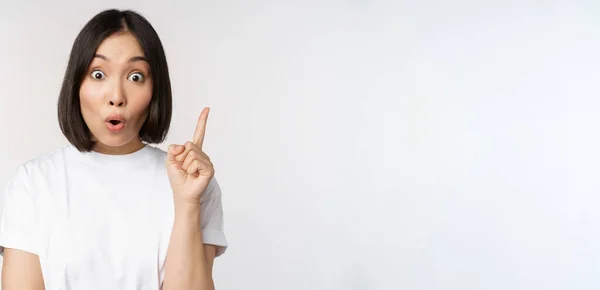 Primer plano de creativo asiático chica levantando dedo, sugiriendo smth, tiene una idea, apuntando hacia arriba, eureka signo, de pie sobre blanco fondo — Foto de Stock