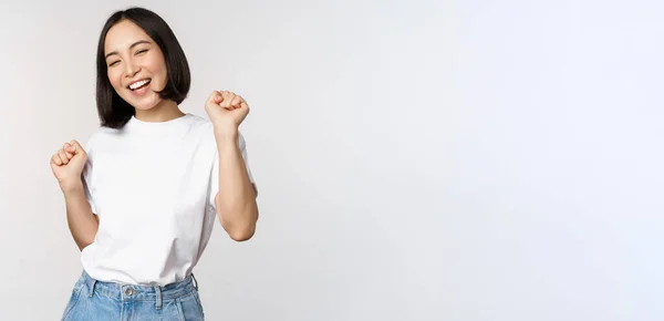 Chica coreana bailando feliz posando sobre fondo blanco, usando camiseta —  Fotos de Stock