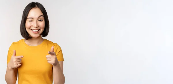 Junge koreanische Studentin, zeigt mit dem Finger in die Kamera und lächelt, gratuliert, wählt, lädt Menschen ein, steht vor weißem Hintergrund — Stockfoto