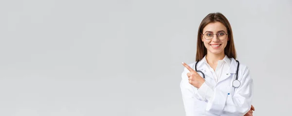 Trabajadores de la salud, medicina y concepto de pandemia covid-19. Doctora profesional guapa en bata blanca y anteojos, señalando con los dedos hacia la izquierda, sonriendo amigable, mostrando información — Foto de Stock