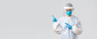Covid-19, virüsün önlenmesi, sağlık, sağlık çalışanları ve karantina konsepti. Kızgın somurtkan doktor ya da hemşire kişisel ekipman, tıbbi kıyafet, solunum cihazı ve eldivenler, kötü haberleri işaret etmek