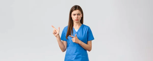 Медичні працівники, запобігають вірусам, страхуванню та концепції медицини. Занепокоєна і стривожена молода жінка-лікар або медсестра в блакитних скрабах, що кидаються тривожним, вказуючи пальці, залишені за важливою інформацією — стокове фото