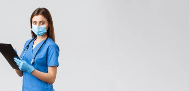 Covid-19, virüsün önlenmesi, sağlık, sağlık çalışanları ve karantina konsepti. Profesyonel kadın hemşire ya da doktor mavi önlüklü, tıbbi maske ve eldivenli hasta bilgilerini not alıyor.