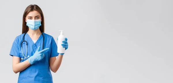 Covid-19，防止病毒、健康、保健工作者和检疫概念。年轻漂亮的女护士或医生，身穿蓝色的刷子，戴着医疗面罩和手套，指着手边的清洁剂、肥皂 — 图库照片