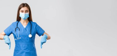 Covid-19, virüsün önlenmesi, sağlık, sağlık çalışanları ve karantina konsepti. Kararlı kadın hemşire ya da doktor mavi önlüklü, tıbbi maske ve eldivenli, parmakları aşağıda, bilgi pankartı gösteriyor