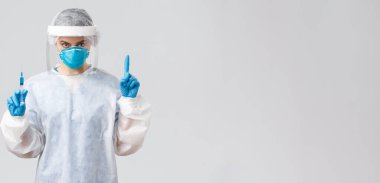 Covid-19, tıbbi araştırma, teşhis, sağlık çalışanları ve karantina konsepti. PPE kostümlü kararlı doktor, kişisel koruyucu ekipman, hasta için koronavirüs aşısı olan şırınga