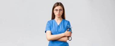 Sağlık çalışanları, ilaç, sigorta ve covid-19 salgını konsepti. Ciddi ve kararlı, profesyonel bayan hemşire, mavi önlüklü doktor, steteskop tutuyor, gözlük takıyor, kendinden emin görünüyor.