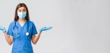 Covid-19, virüsün önlenmesi, sağlık, sağlık çalışanları ve karantina konsepti. Şaşırmış ve heyecanlı kadın hemşire ya da doktor mavi önlüklü ve tıbbi maskeli, yan yana eğlenerek ellerini uzat