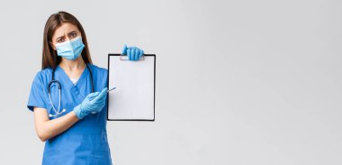 Covid-19, virüsü önleme, sağlık çalışanları ve karantina konsepti. Endişeli kadın hemşire ya da doktor mavi önlüklü, tıbbi maskeli, Coronavirus sırasında maske ve eldiven kullanmanın önemini açıklar.