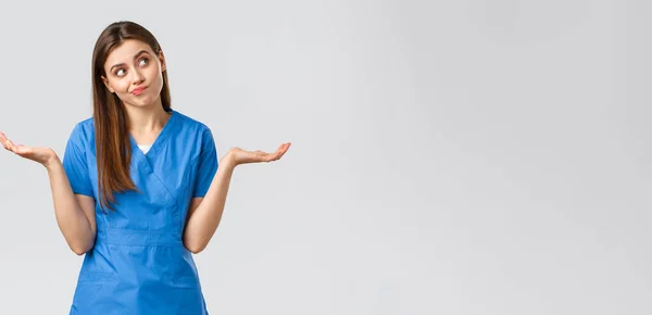 Trabajadores de la salud, prevenir virus, seguros y concepto de medicina. Médico atractivo indeciso y despistado, enfermera vestida de azul, encogiéndose de hombros con las manos de lado y sonriendo, apartar la mirada — Foto de Stock